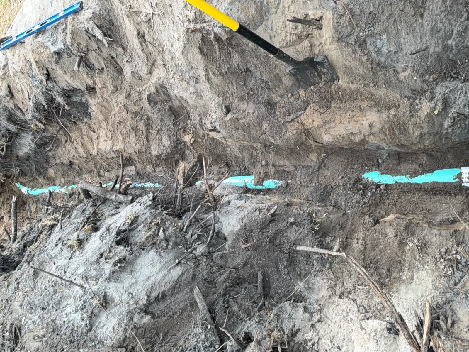 New green PVC sewer line along the bottom of an open trench with a shovel and level