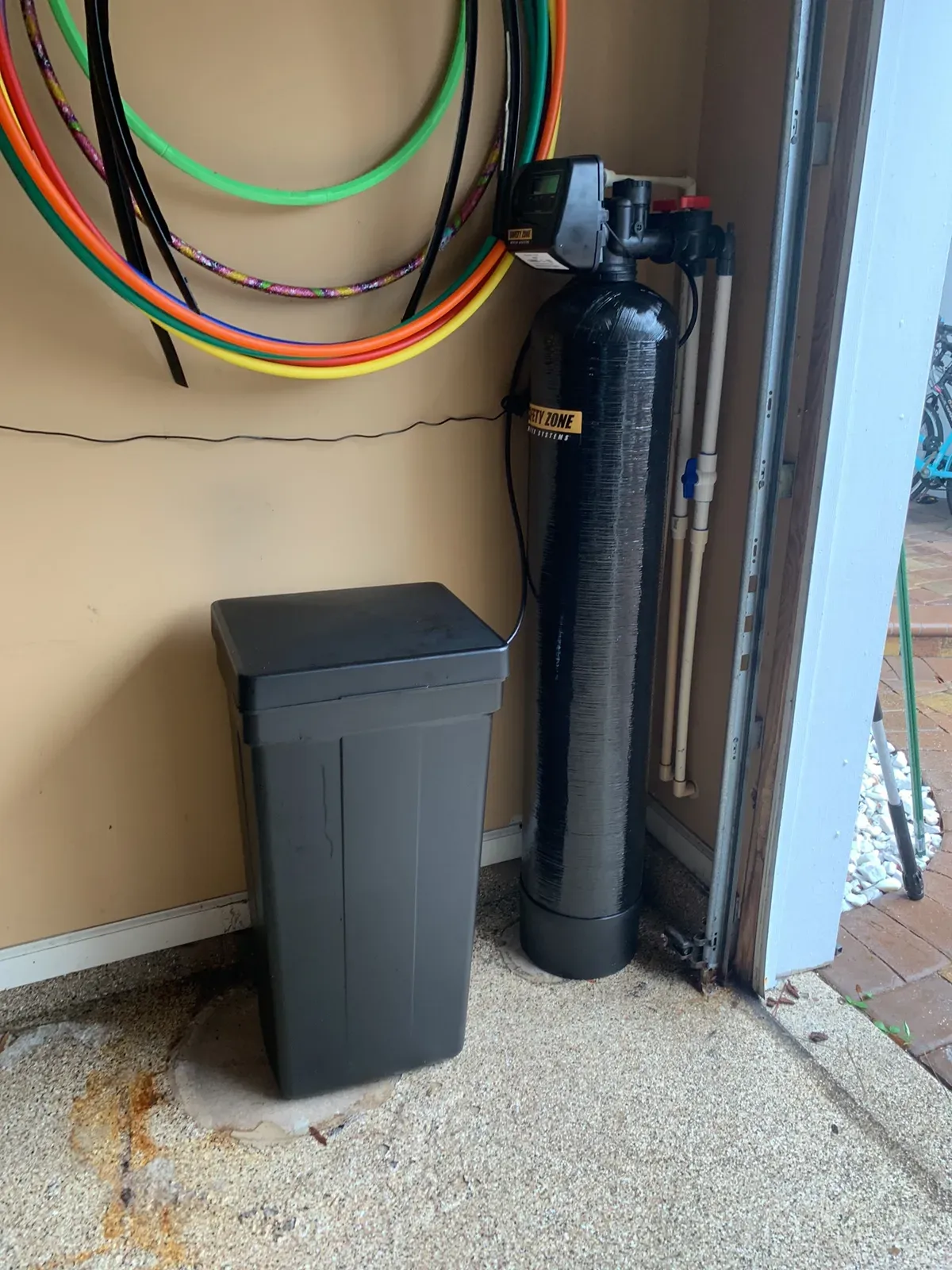 Water softener tank with control head next to a brine tank, installed in a garage corner